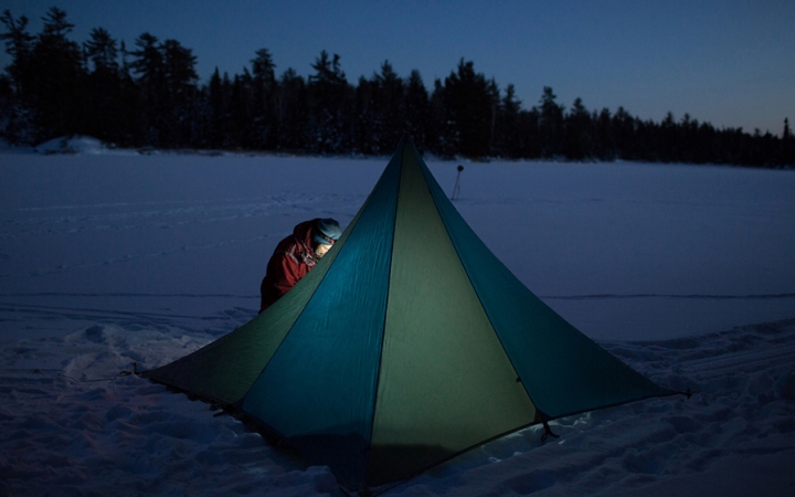 a tent resting on a snowy landscape is illuminated by a person's headlamp